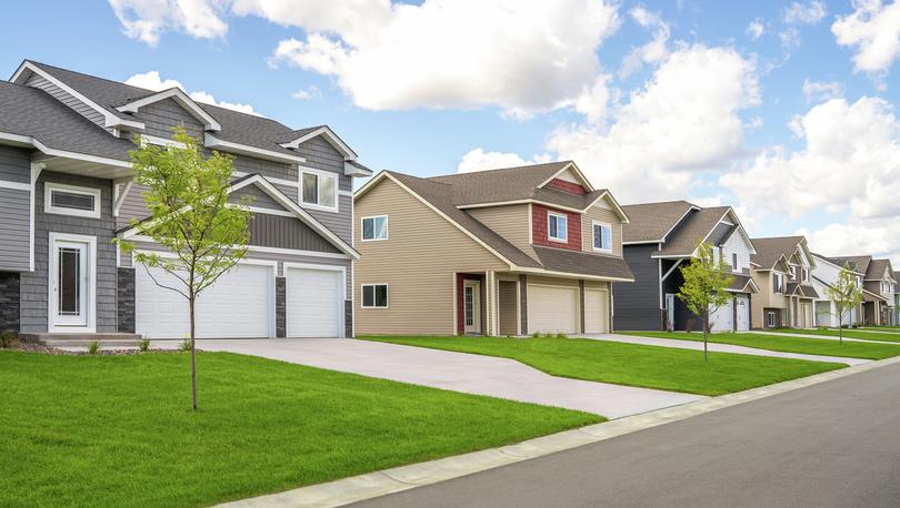 Streetline photo of several two-story homes with 3-car garages, green lawns and asphalt street.