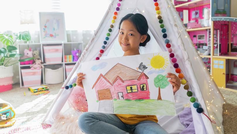 Stock image of girl in her bedroom coloring a picture of a house.