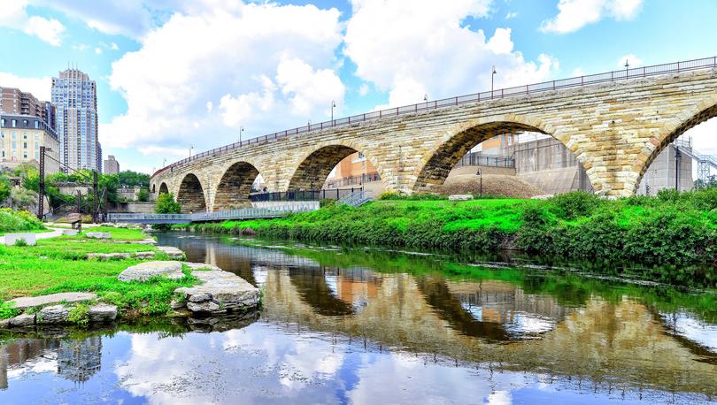 Minneapolis, Minnesota downtown showing Stone Arch Bridge, still water in the river, and tall city buildings off in the background