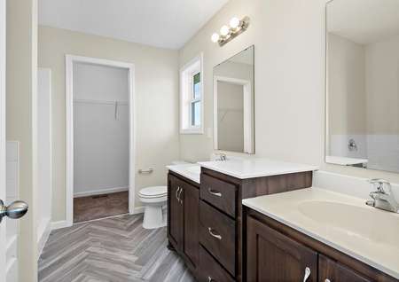 Photo of primary bathroom with a split vanity, decorative tile flooring and access to a walk-in closet.
