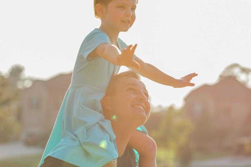 Little girl on dad's shoulders with arms out.