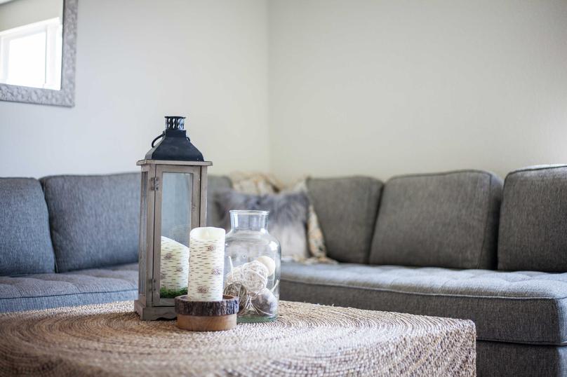 Staged living room with grey couch and white colored coffee table with vase and candle sitting on it.