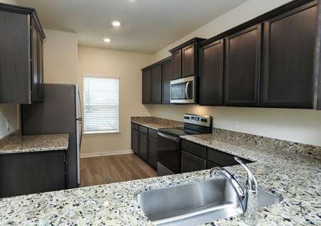 view of kitchen from breakfast bar, granite counters, stainless electric range, builtin microwave, refrigerator and window