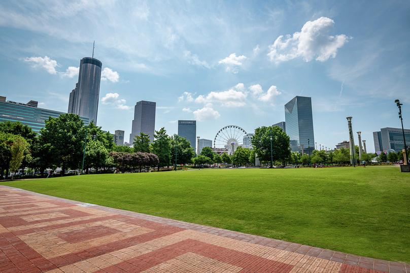 Atlanta, Georgia cityscape showing beautiful green grass park in the front, skyscrapers in the distance, and blue cloudy skies in the background