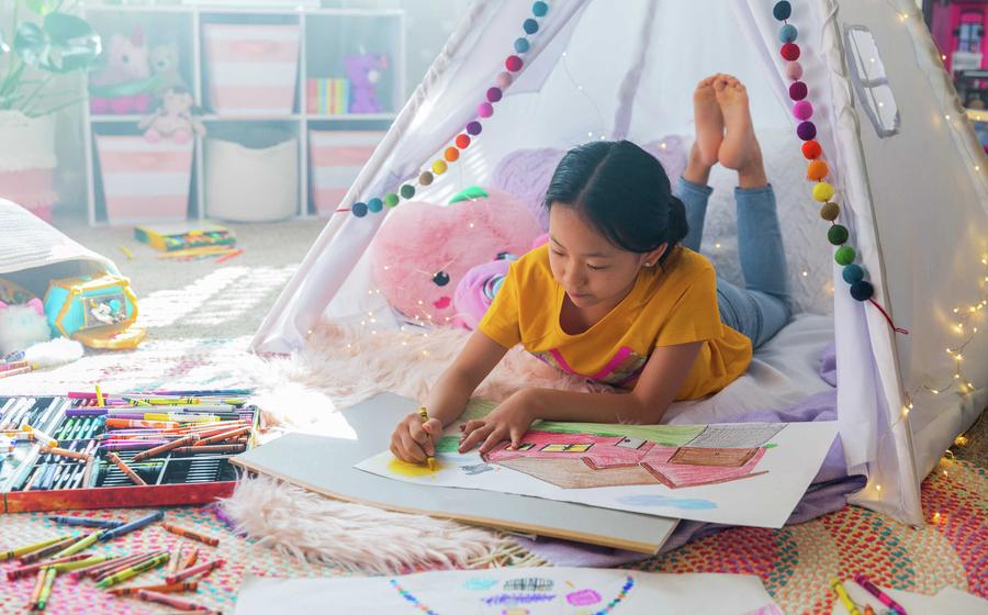 Young girl coloring with crayons in a colorful room.