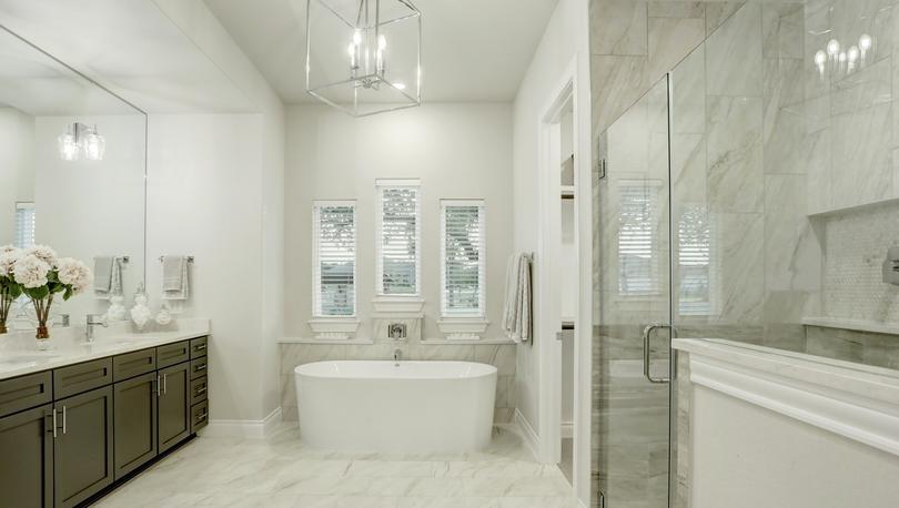 Staged master bath with white freestanding tub, luxury lighting and white tile floors.