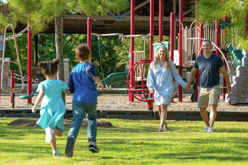 Two children running toward smiling parents at a community park. 