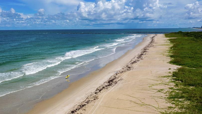 Fort Pierce, Florida beach with single surfer holding a yellow surfboard and rolling waves hitting light brown sands