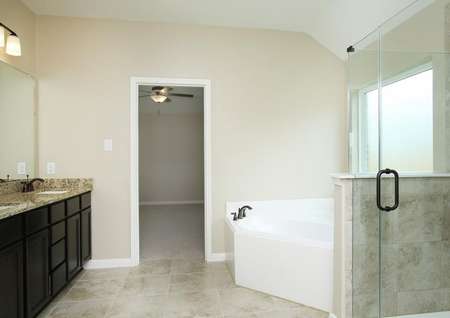 The luxurious master bathroom of the Hendrie includes a corner soaking tub, frameless glass shower, and a granite dual-sink vanity with decorative light fixture.