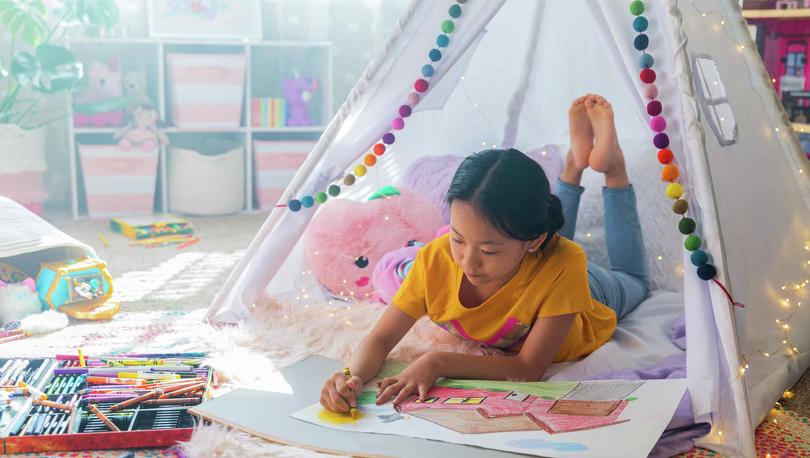 Young girl coloring with crayons in a colorful room.