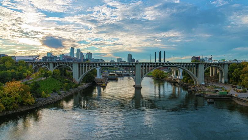 Minneapolis, Minnesota bridges going across the Mississippi River and showing boats, plants lining the banks, and skyscrapers off in the distance