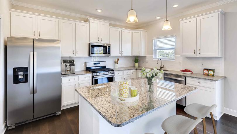 Persimmon model home completed with modern stainless steel refrigerator, stove, and microwave, brown stone countertops, and dark brown wood like ceramic floors