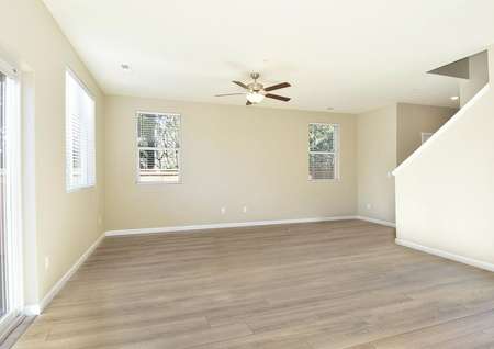 Spacious family room with three windows, a ceiling fan, plank flooring, a sliding glass door and view of staircase.