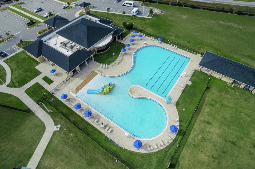 Drone view of the Poinciana community pool area that is surrounded by grass fields and some buildings.