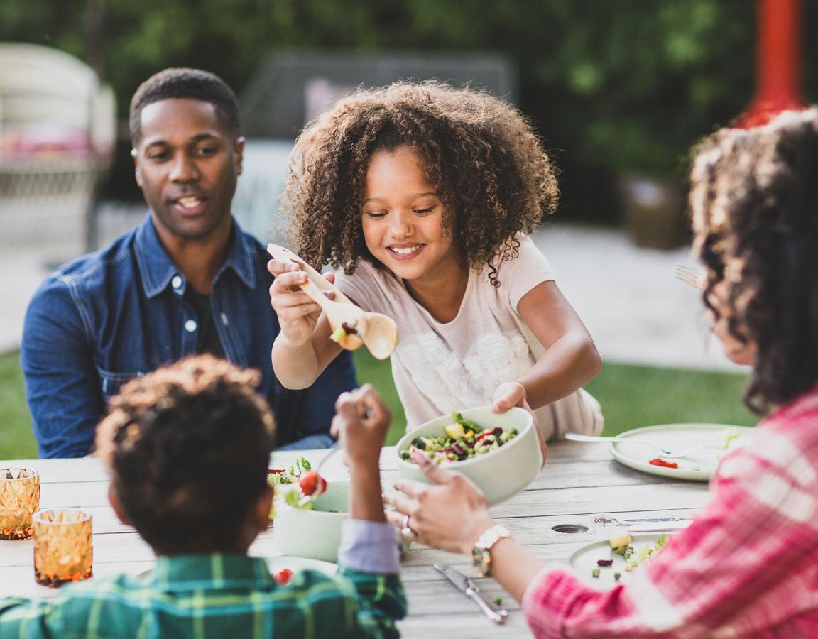 A girl serves salad to her family at the dinner table.