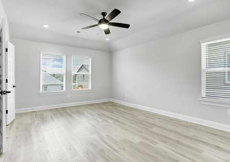 Spacious master bedroom with large windows, a ceiling fan, and wood flooring. 