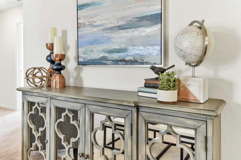 Model home with a seascape painting on the wall plus a globe, books, and candles sitting on a decorative wooden credenza with mirrored doors