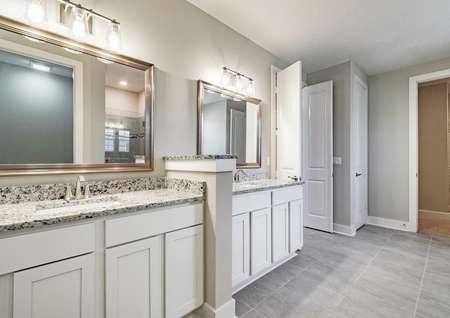 Master bathroom with split vanity, granite countertops, white cabinetry, two framed mirrors and tile flooring.
