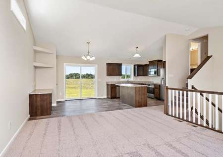 Photo of open entertaining area with a large family room with carpet, a spacious dining area with a built-in desk and shelving, and a kitchen with an island and brown cabinets.
