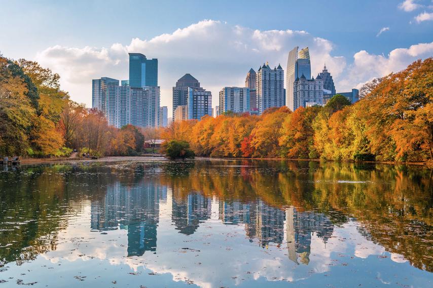 Atlanta, Georgia Piedmont Park showing the city's skyscrapers in the distance, still lake water, and trees with Autumn leaves lining the banks