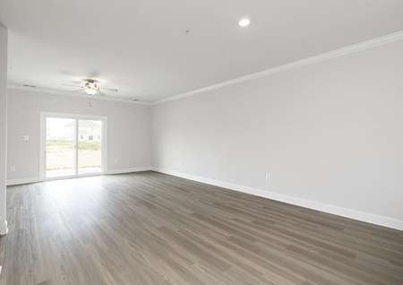 Spacious open family room with plank floors, a ceiling fan and a sliding glass door the back yard.