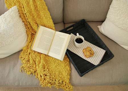 Staged living room with book, coffee cup, and yellow shawl on couch.