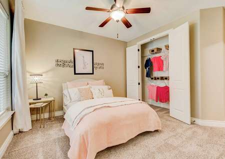 Mantle kid's bedroom with peach sheets on bed, brown ceiling fan, and open closet with clothes