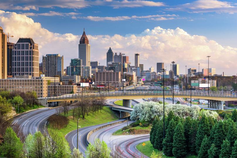 Atlanta, Georgia Downtown Skyline featuring numerous skyscrapers and office buildings, cars driving on the freeways, and blue skies with white clouds