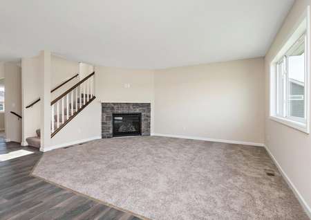 Photo of a carpeted living room with a corner fireplace and view of stairs leading up to the second floor.