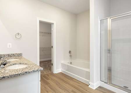 Primary bathroom with plank floors, granite vanity with two sinks, a garden tub and step-in shower.