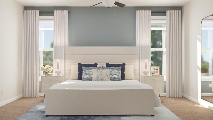 Rendering of the spacious master suite in
  the Anna floor plan, which has two windows, a ceiling fan and carpeted
  flooring. The space is decorated with a large bed, two nightstands, a blue
  rug and a mirror.