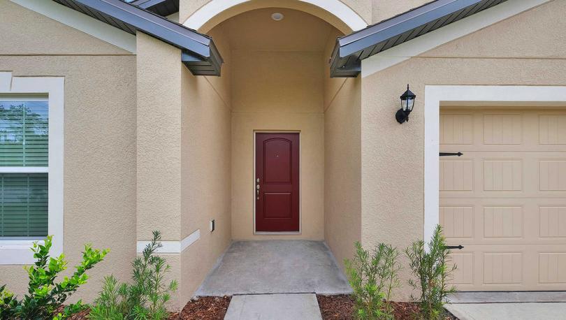 Close up view of a home's exterior showcasing beautiful landscaping and a red door. 