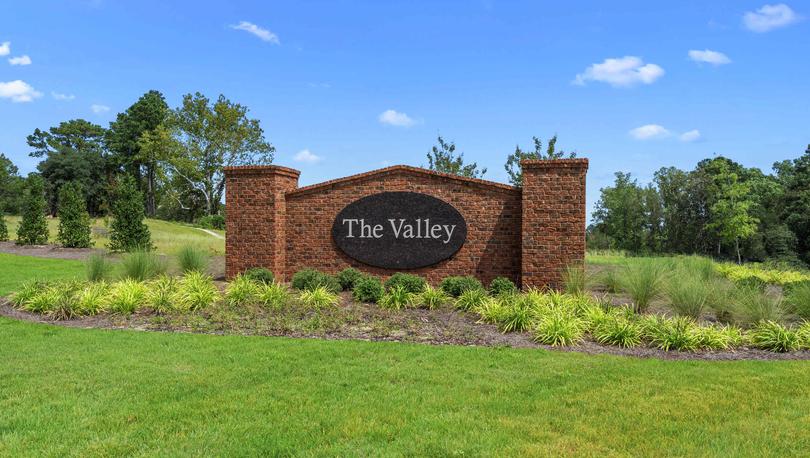 The Valley community sign with the words The Valley in white on a black background surrounded by plants and lush green grass.
