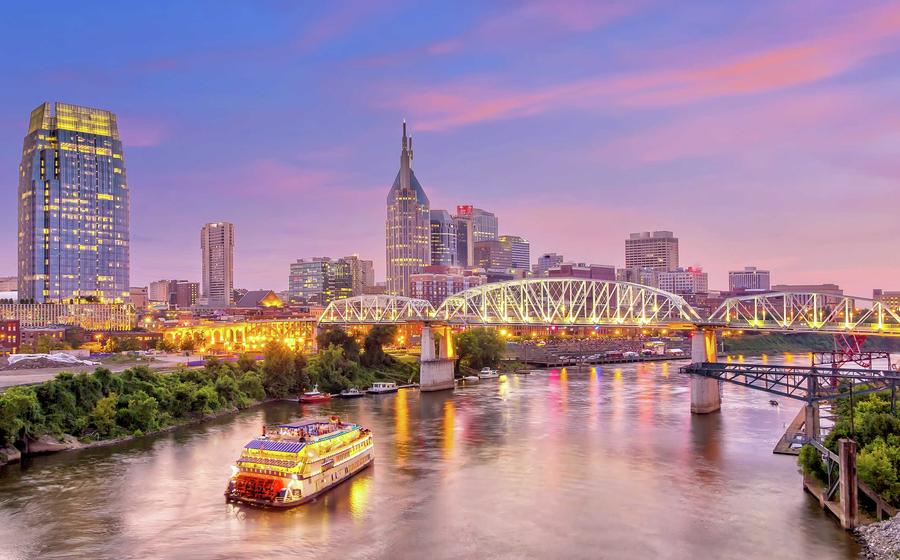 Nashville, Tennessee cityscape taken from across the Cumberland River showing flowing water, green grass, and tall office buildings in the distance