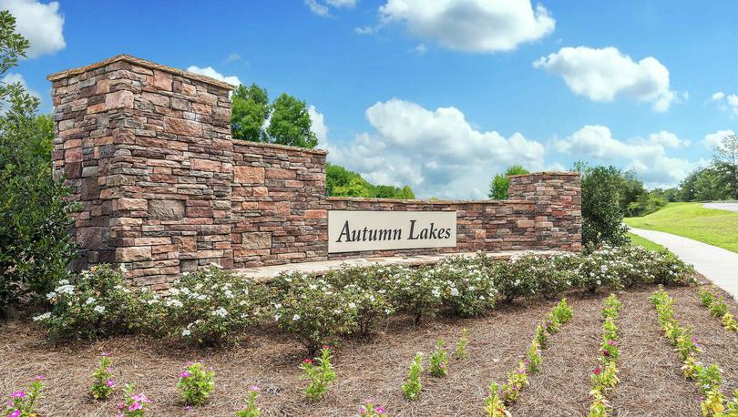 Brick entrance sign with the words Autumn Lakes in black on a white background.