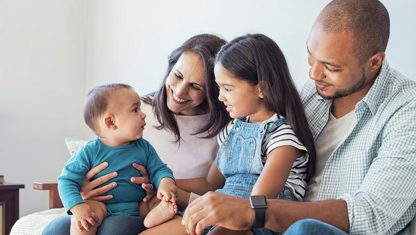 Multi-ethnic family at home with happy baby son and little girl relaxing together on sofa at home.