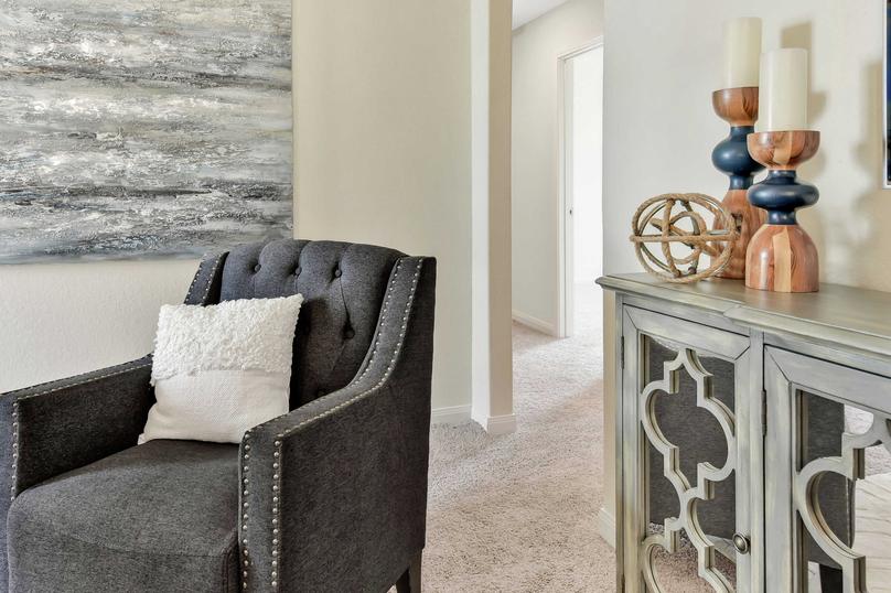 This home is staged with furniture including a dark gray chair with white pillow, wooden entertainment center, and artwork hanging on the wall.