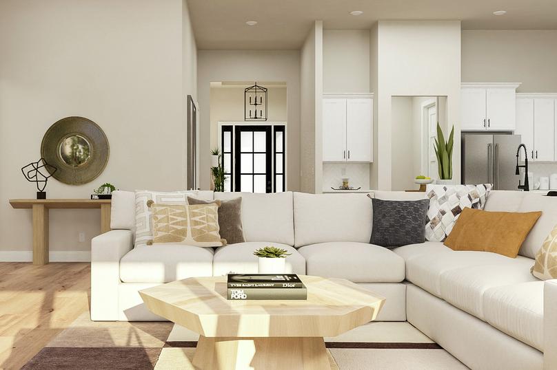 Rendering of the living area showing a
  large white sectional and coffee table, a view of the kitchen in the
  background, and light wood flooring throughout.