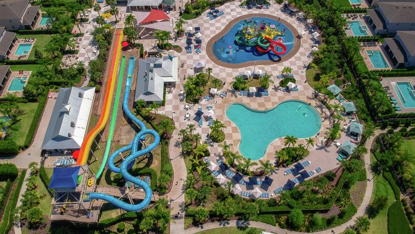 Drone shot overlooking 10-acre water park with water slides, a children's playground with splash pad, a swimming pool and multiple dining options. 