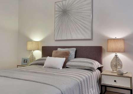 Bed with gray linens, side tables with lamps and a decorative wall hanging.