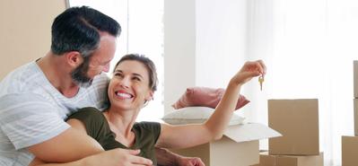 Happy middle-aged couple sitting on floor near moving boxes holding keys