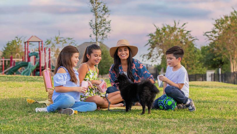 Smiling family sitting down on a field with a small dog. 