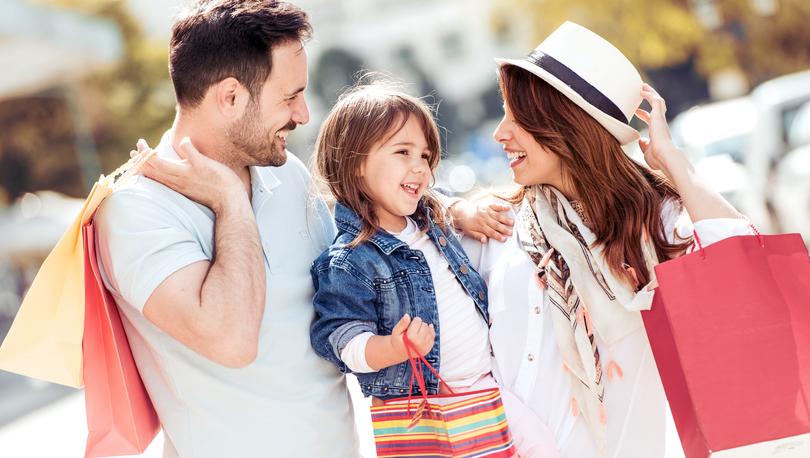 Stock photo of a smiling, trendy couple and daughter outdoors in the sunshine carrying shopping bags.