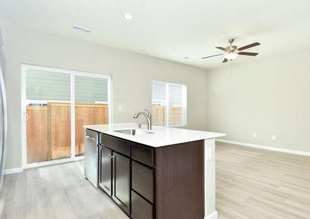 Photo of the open kitchen with island and family room with ceiling fan.
