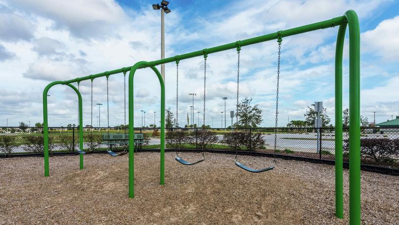 A children's play area in the Poinciana community that has a green swing set and a bench to the side.