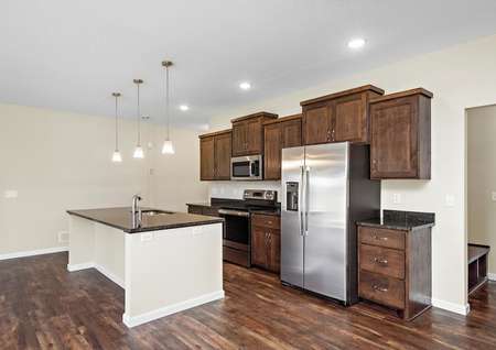 Photo of a kitchen with brown cabinets, stainless appliances and a spacious island with granite counters and pendant lights.
