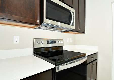 Closeup photo of the electric range and quartz countertops with dark cabinets.