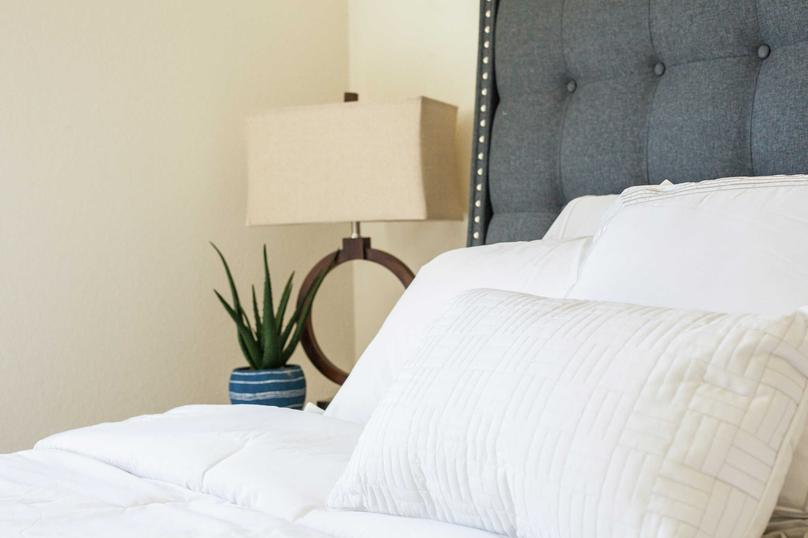 Home staged with bedroom furniture including bed with white sheets, grey headboard, and modern lamp