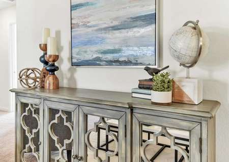 Walnut model home with a seascape painting on the wall plus a globe, books, and candles sitting on a decorative wooden credenza with mirrored doors