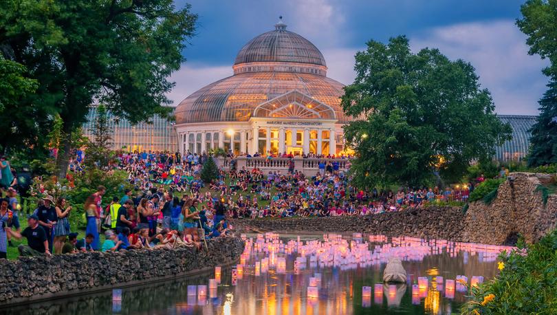 Minneapolis, Minnesota Como Park during Japanese festival with numerous lanterns in the water, people standing on the shores, and large glass dome building in the back